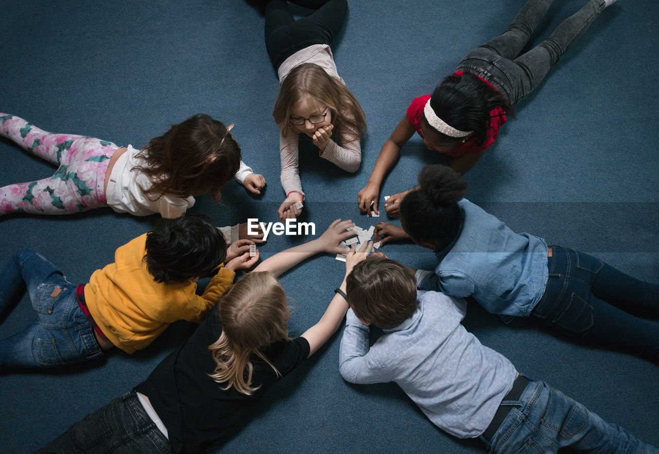 Directly above shot of children playing while lying on floor in school