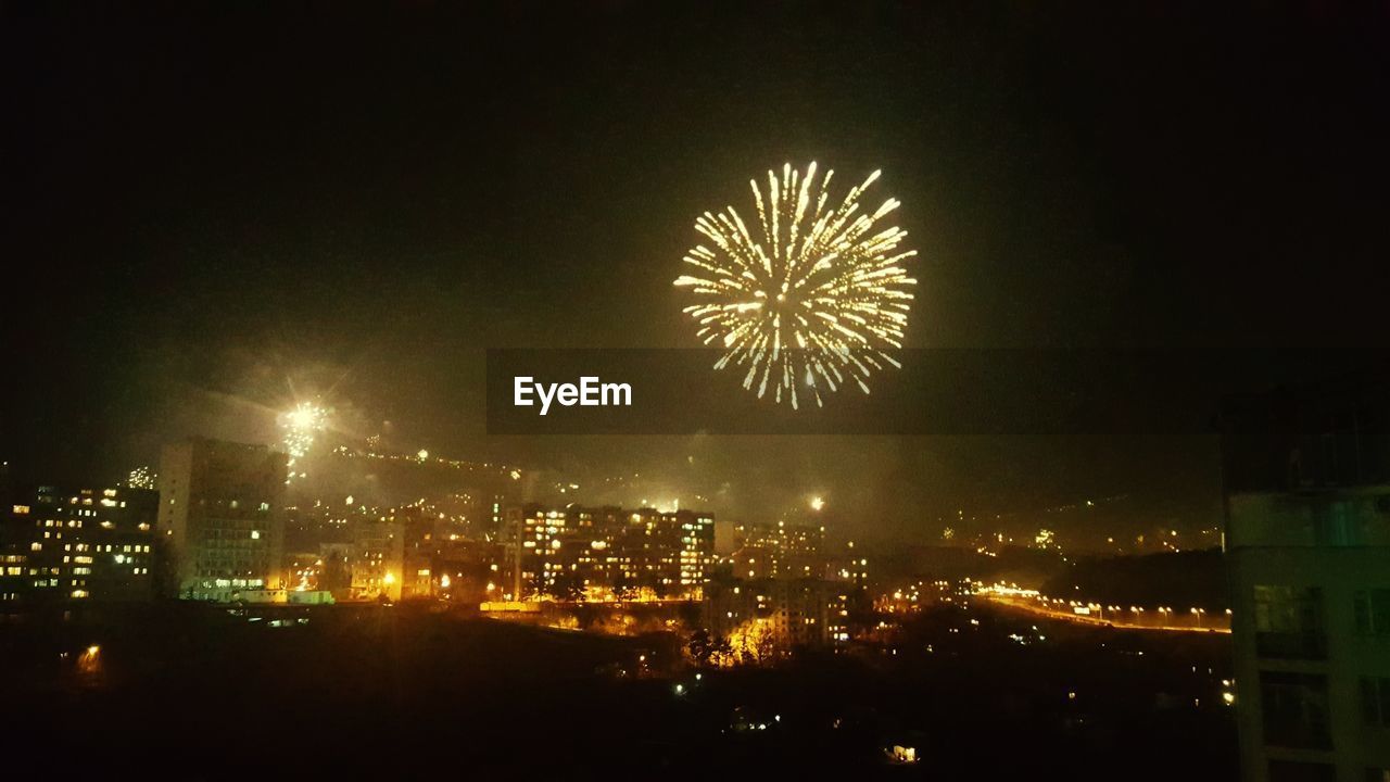 LOW ANGLE VIEW OF FIREWORK DISPLAY OVER CITY AT NIGHT