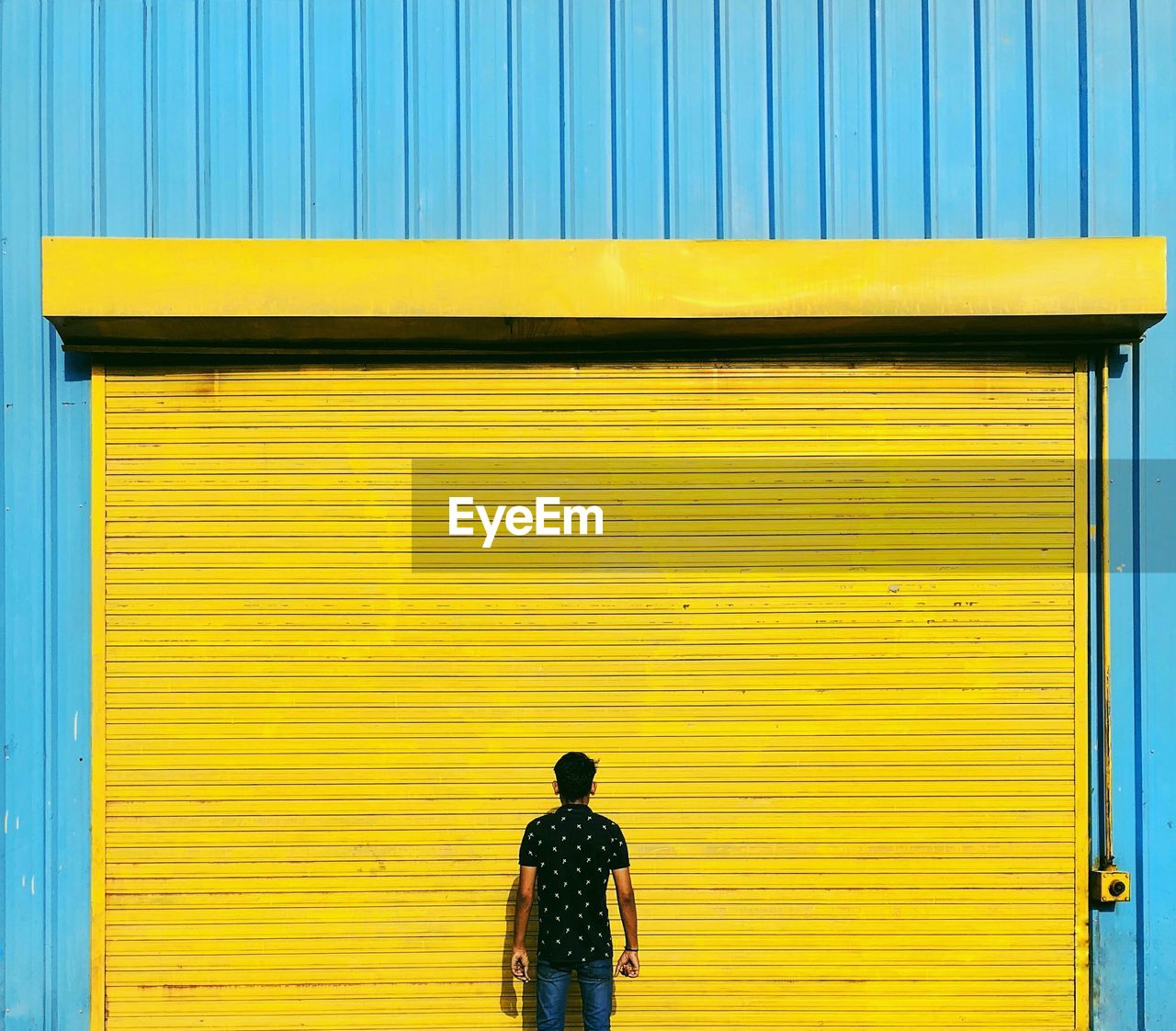 Rear view of man standing against closed yellow shutter
