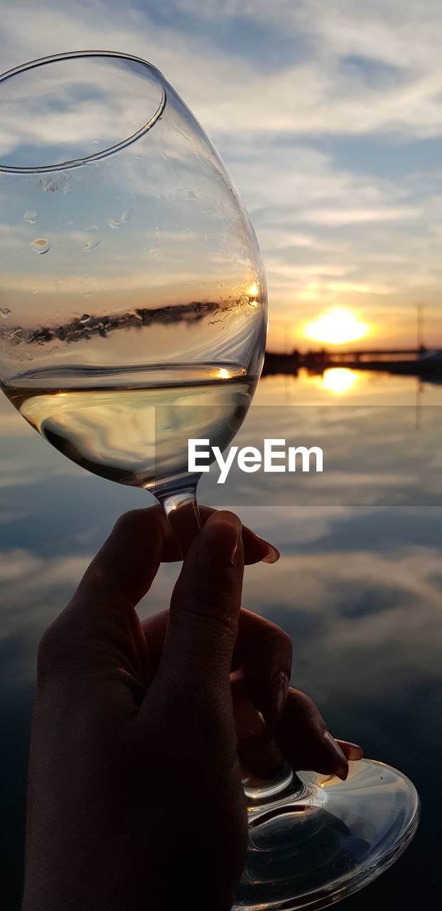 CLOSE-UP OF PERSON HOLDING GLASS AGAINST SKY DURING SUNSET