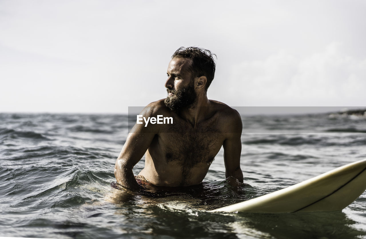 Young man surfboarding in sea against sky