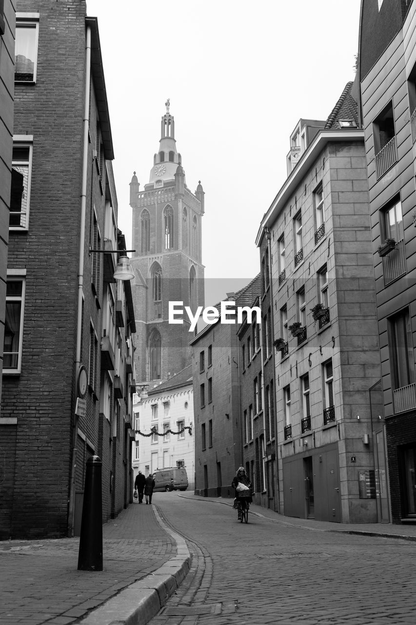 PEOPLE WALKING ON STREET AMIDST BUILDINGS IN CITY AGAINST SKY