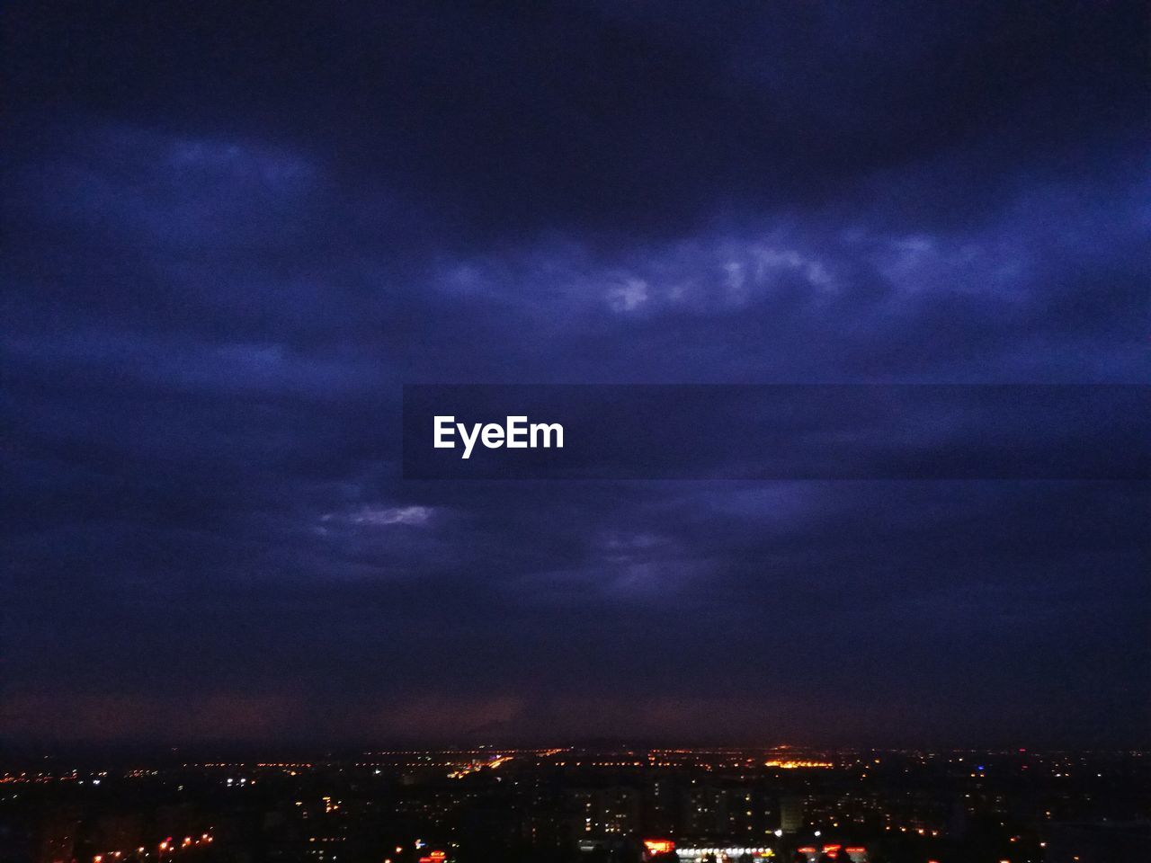 AERIAL VIEW OF ILLUMINATED CITYSCAPE AGAINST STORM CLOUDS