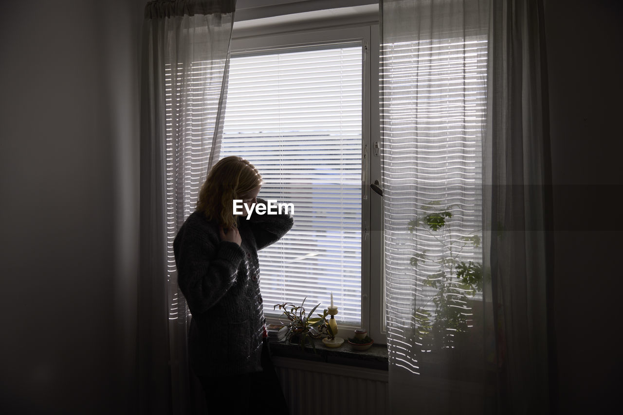 Pensive teenage girl looking through window