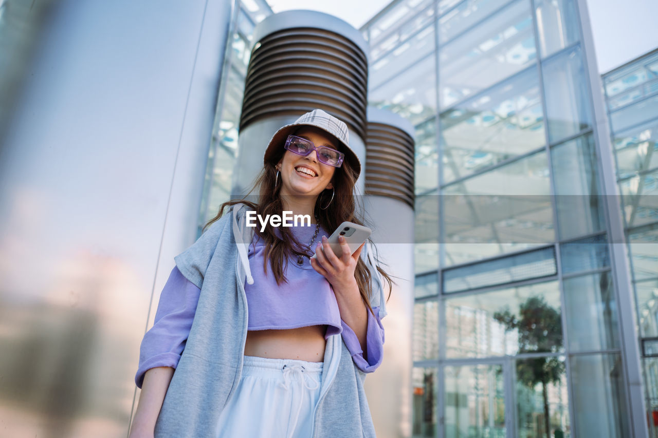 Young cool girl holding and using mobile phone. smiling woman texting with friends