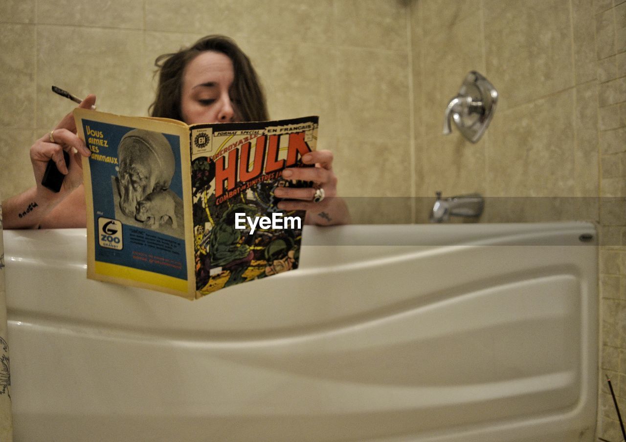 YOUNG WOMAN READING BOOK IN BATHROOM