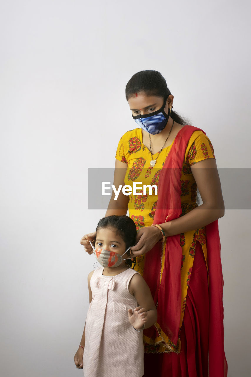 Mother and daughter wearing flu mask standing against white background