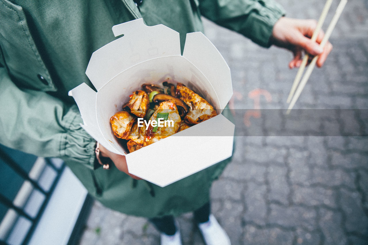 Midsection of person holding street food on sidewalk