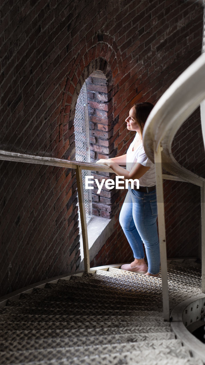 Side view of woman looking through window while standing on staircase