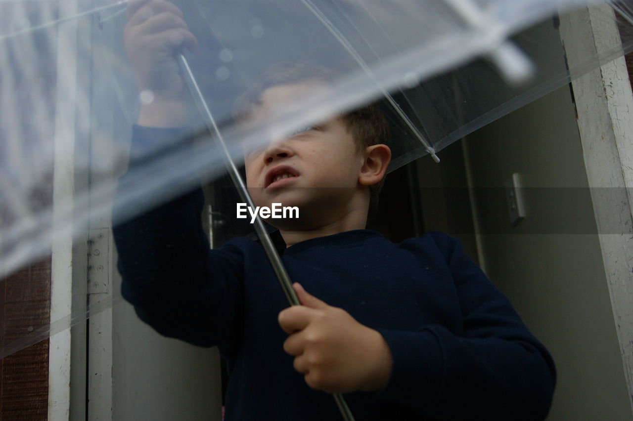 Low angle view of boy holding transparent umbrella