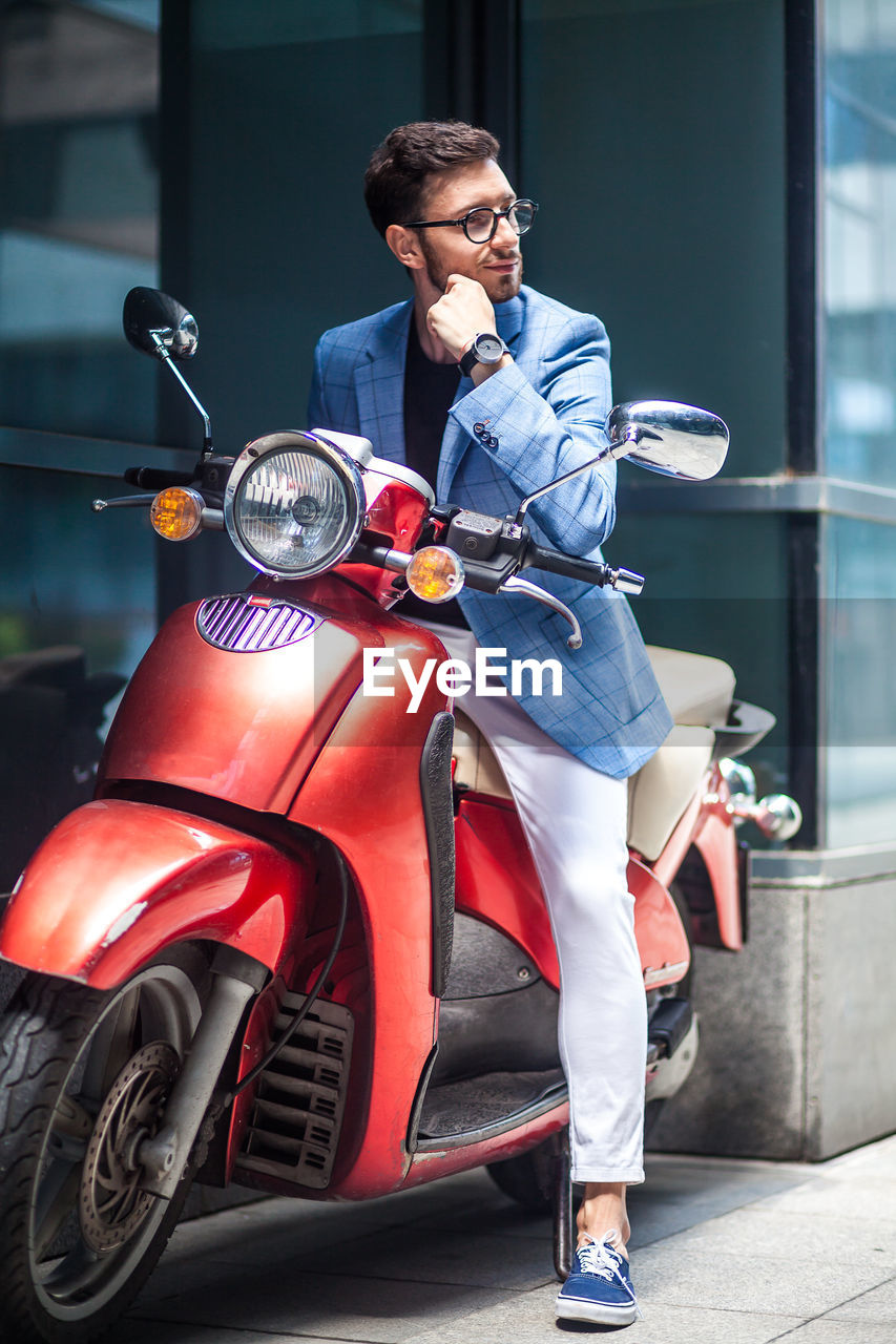 Young businessman looking away while sitting on motor scooter
