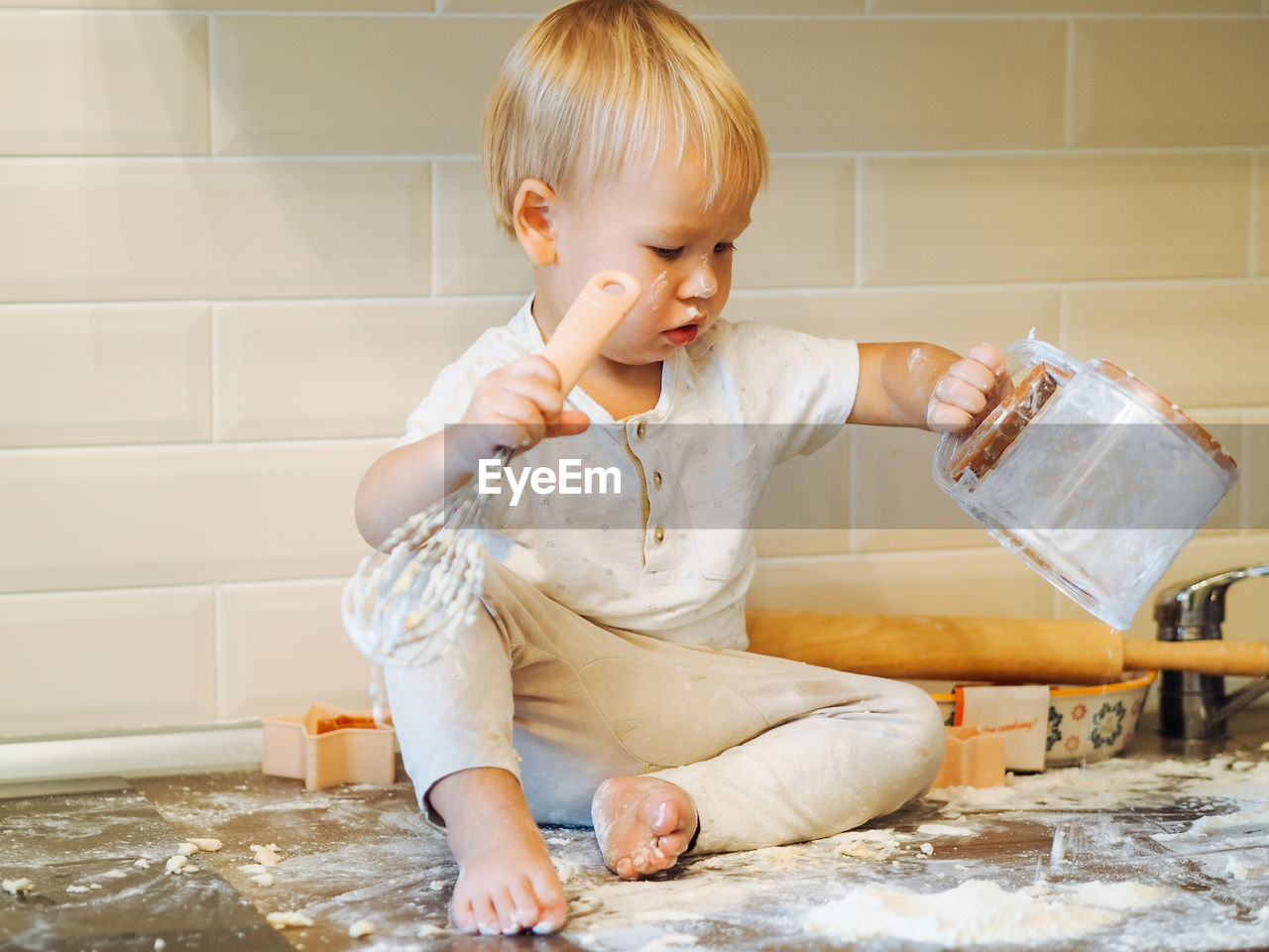 Cute toddler playing with flour at kitchen