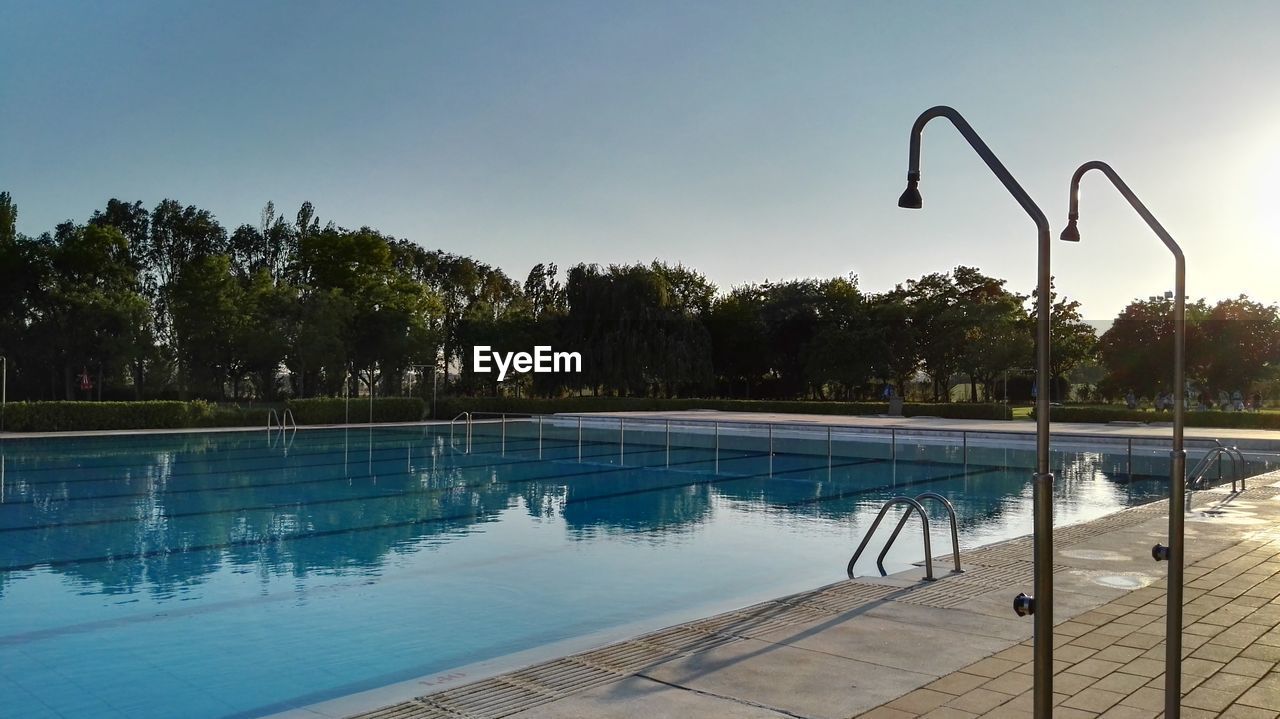 Swimming pool and showers by trees against clear sky