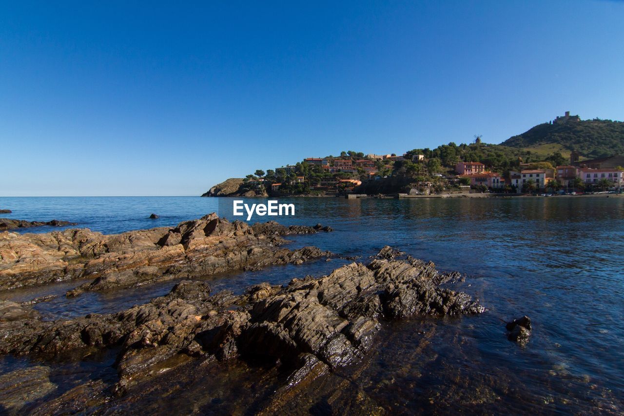 Rocks on sea against clear blue sky