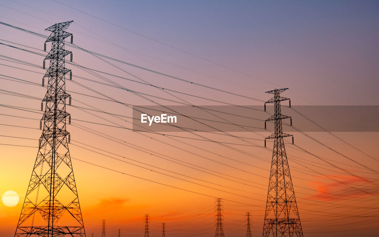 Low angle view of electricity pylon against sky during sunset.