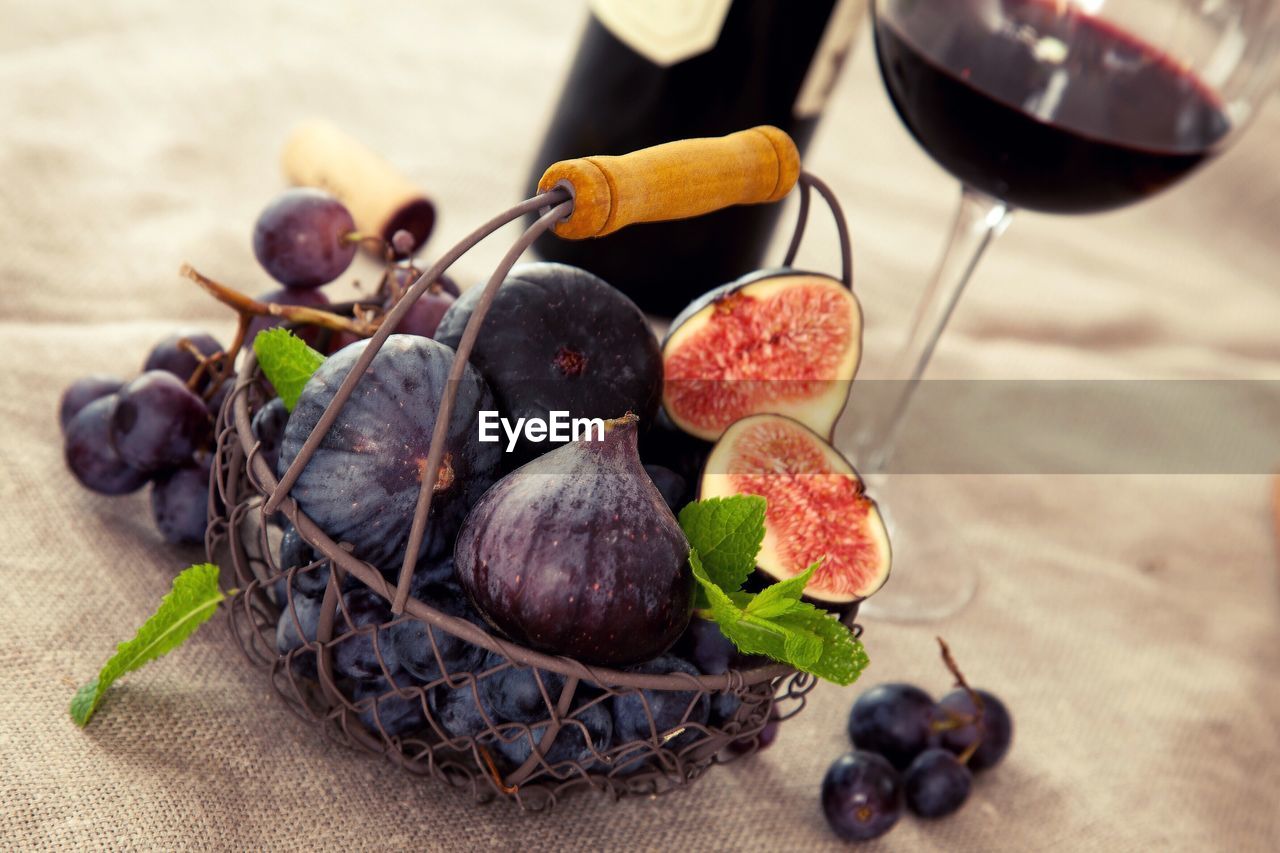 High angle view of figs and grapes in basket by red wine on table