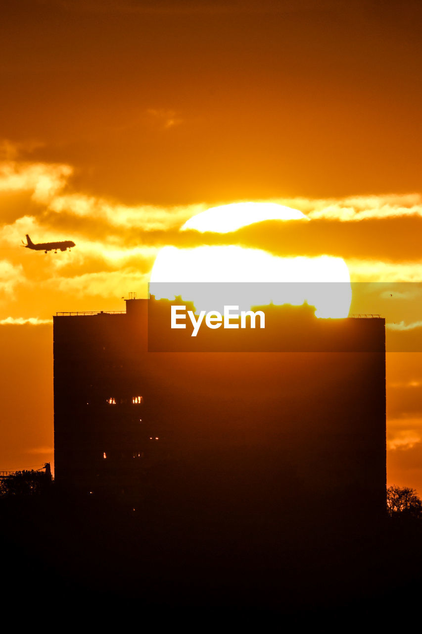 sunset, sky, horizon, silhouette, afterglow, dawn, sun, cloud, architecture, orange color, sunlight, nature, flying, building exterior, built structure, no people, city, evening, beauty in nature, dramatic sky, outdoors, building, air vehicle, bird, airplane, animal themes, animal, landscape, environment, transportation, cityscape, scenics - nature