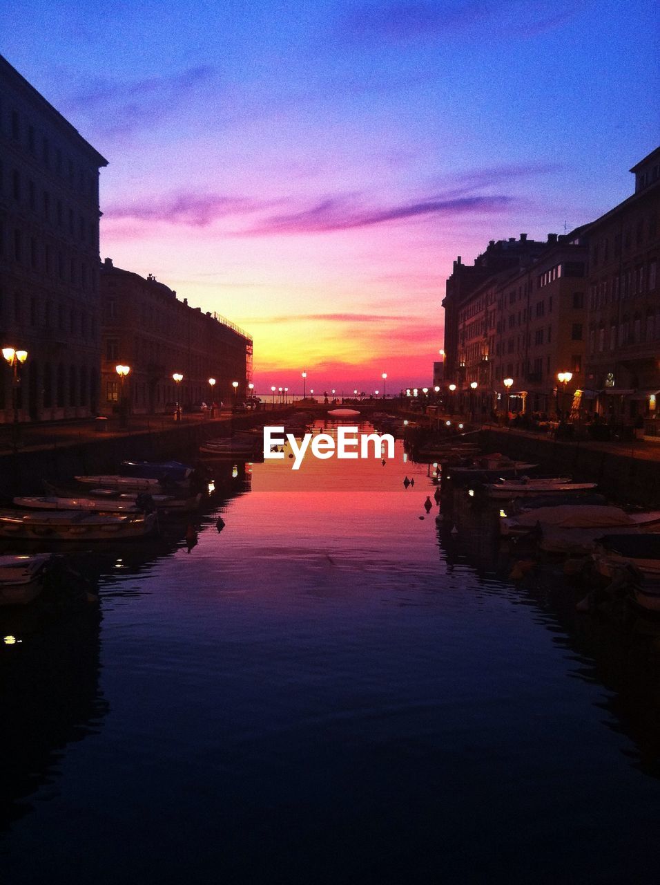 Canal surrounded by buildings against sky during sunset