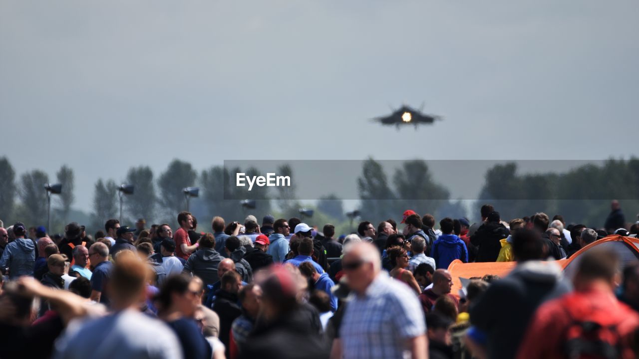 Crowd watching military airplane flying in sky