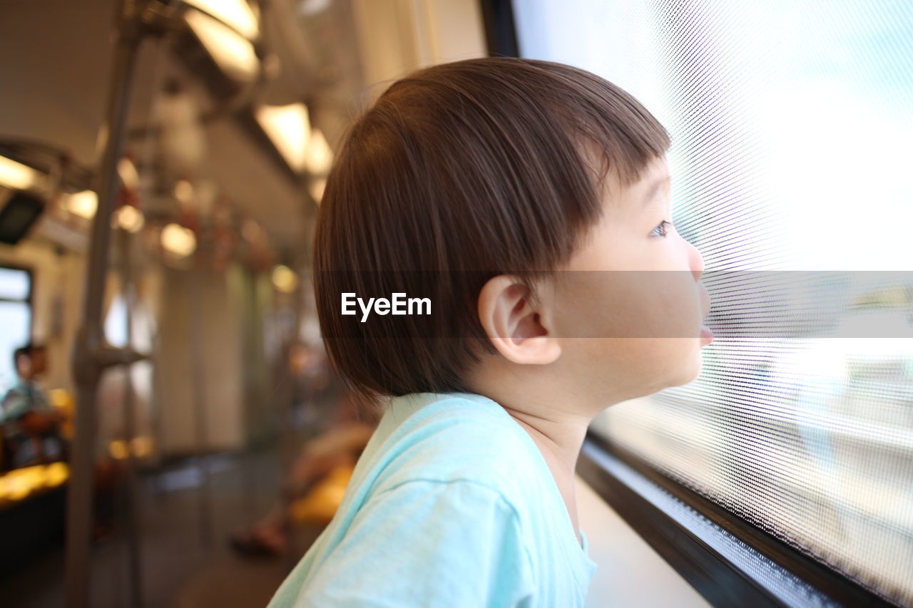 Side view of boy looking through window in train