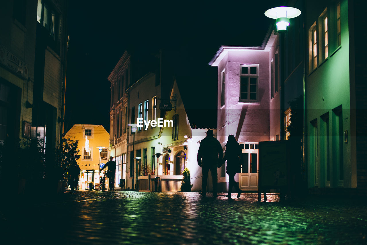 Silhouette couple walking on street amidst houses at night