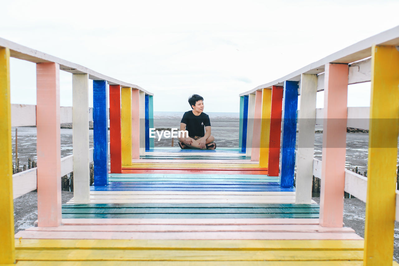 Full length of woman sitting on multi colored pier against sky