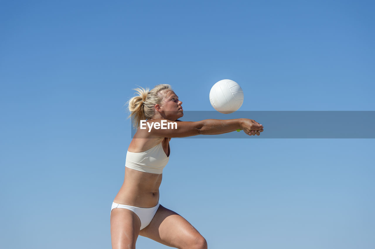 Low angle view of woman playing with ball against clear blue sky