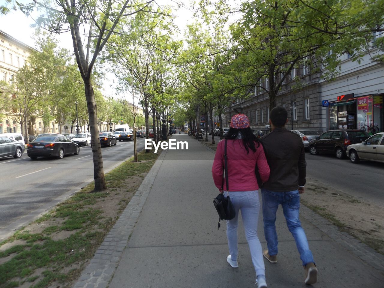 Rear view of couple walking on road along trees