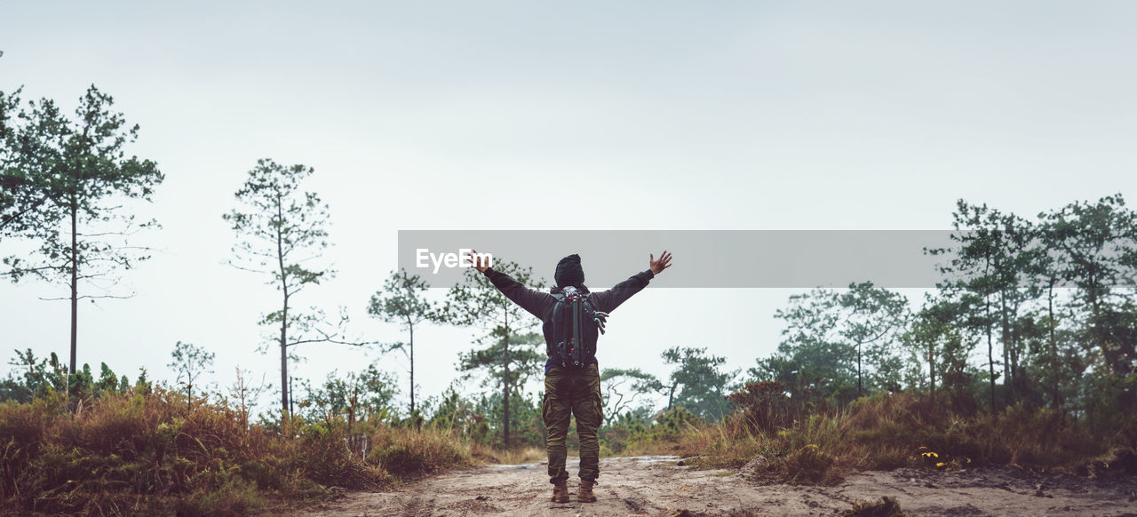 arm, one person, tree, limb, sky, arms raised, plant, nature, human limb, standing, full length, adult, arms outstretched, land, leisure activity, day, environment, outdoors, lifestyles, holiday, landscape, rear view, copy space, young adult, vacation, trip, happiness, carefree, emotion, casual clothing, men, tranquility, beauty in nature, vitality