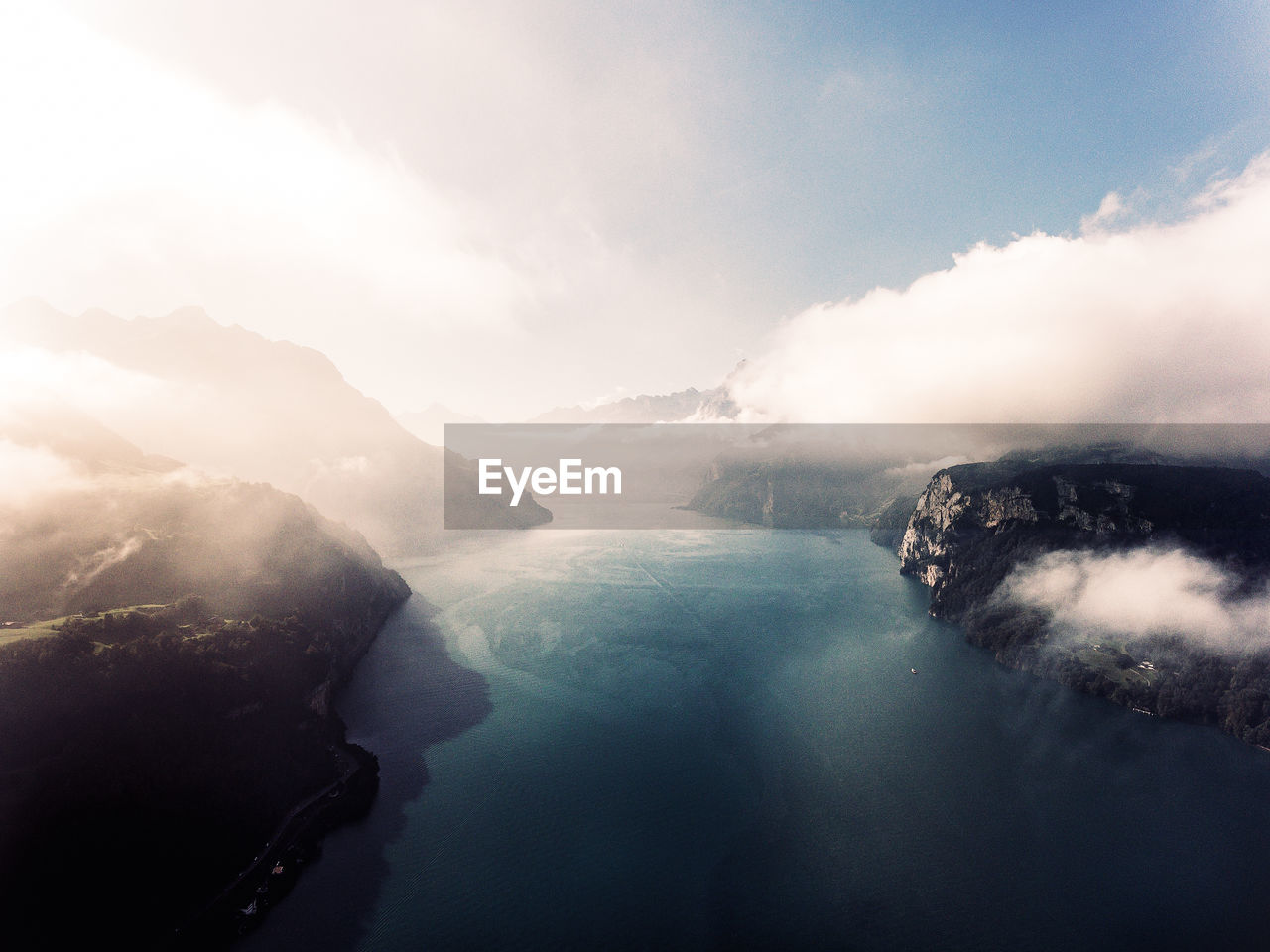 Idyllic shot of river amidst mountains against sky in foggy weather