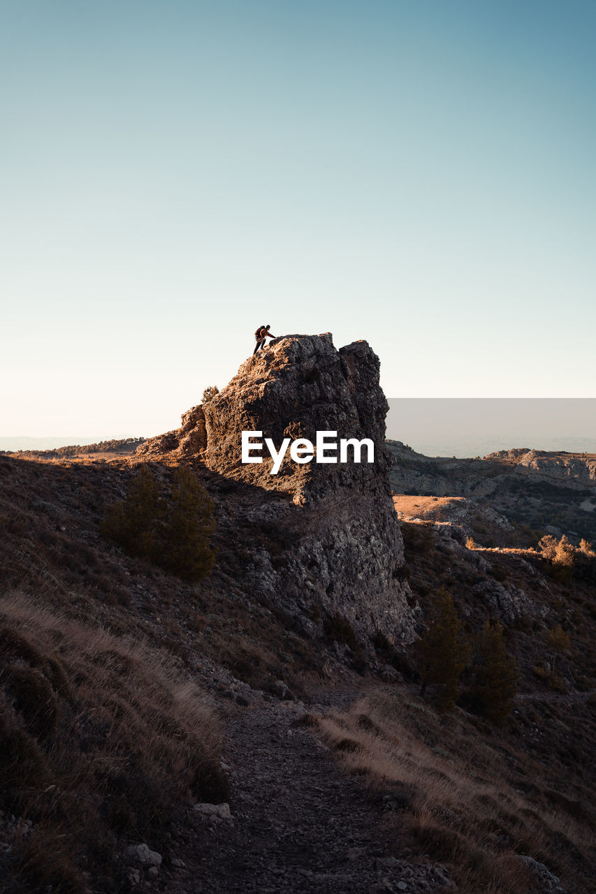 Distant view of man climbing on mountain against clear sky