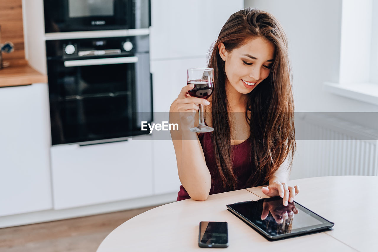 YOUNG WOMAN USING PHONE WHILE SITTING AT HOME