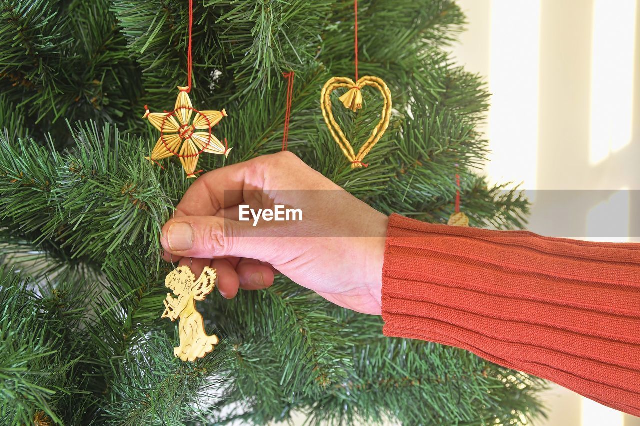 Decorating christmas tree, hand putting christmas decorations on branches. christmas hanging