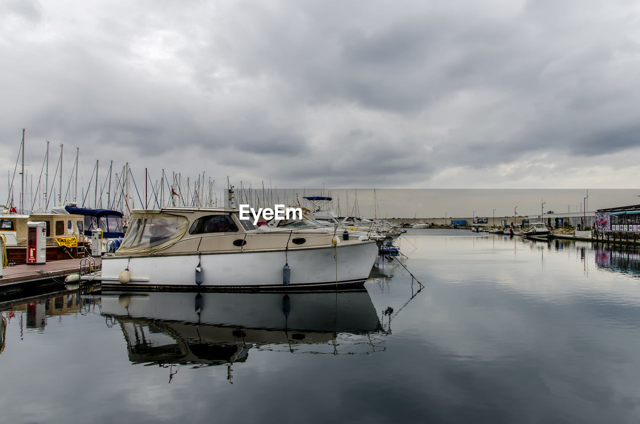 Sailboats moored at harbor against cloudy sky