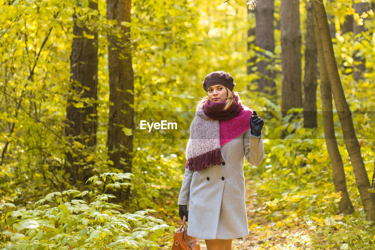 WOMAN STANDING BY TREE TRUNKS IN FOREST