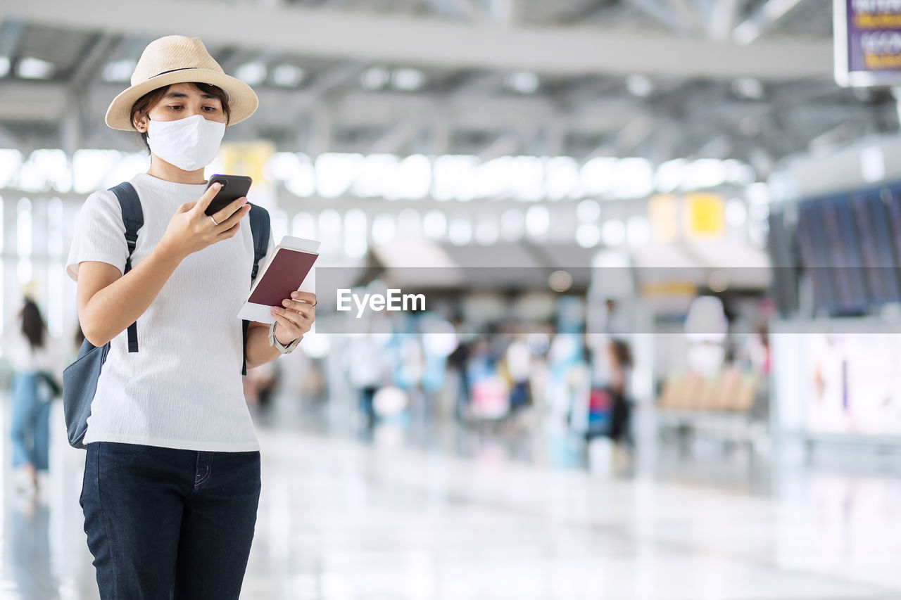 Woman wearing mask using phone standing at airport