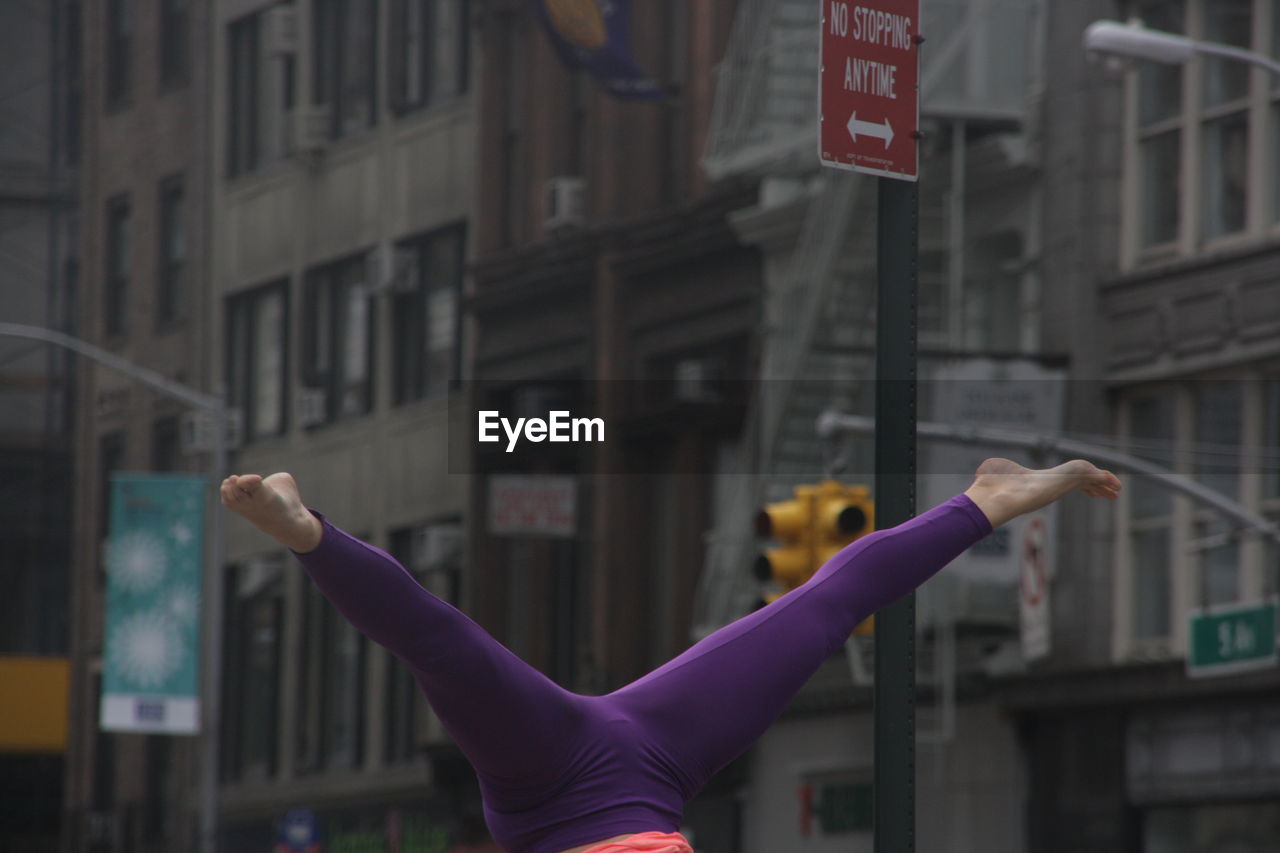 Low section of woman doing split handstand against buildings