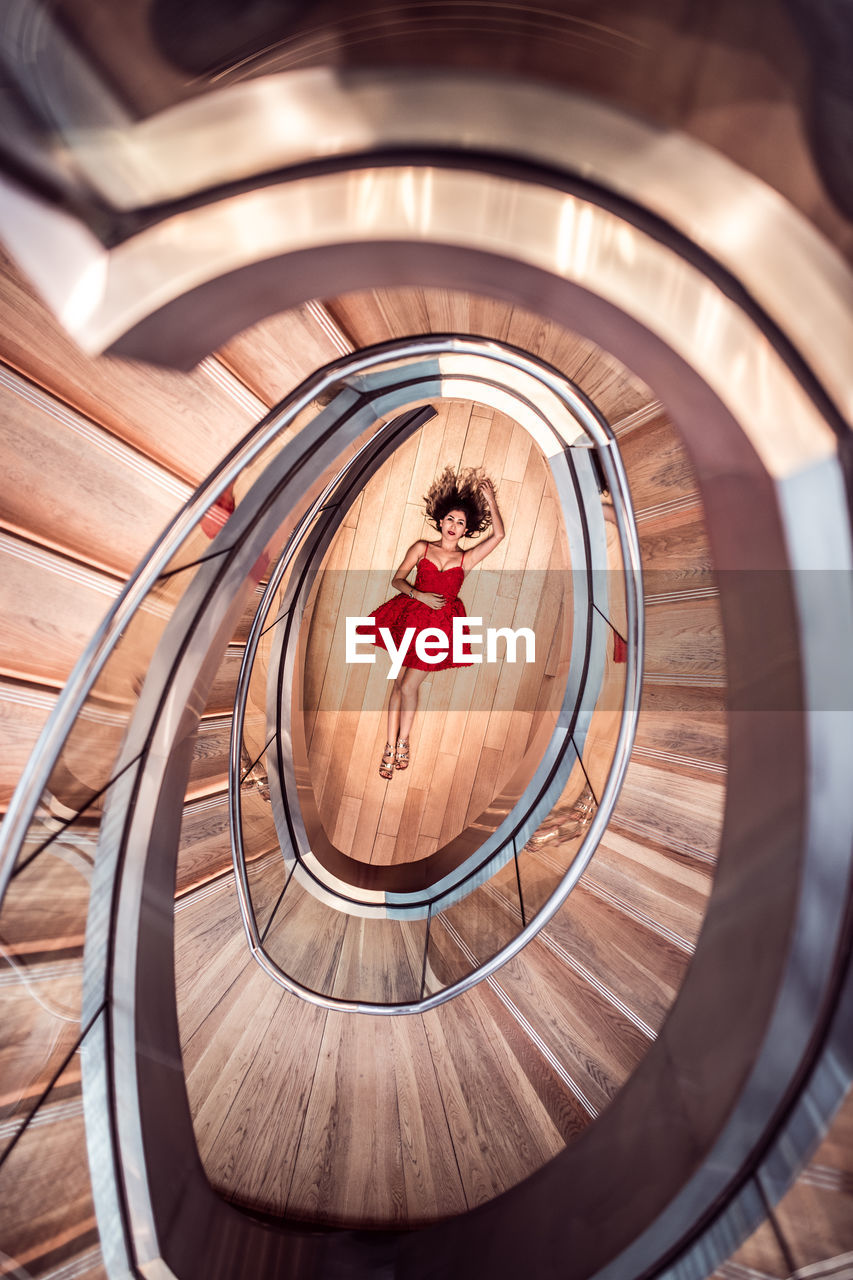 Directly above shot of woman lying on floor amidst spiral staircase