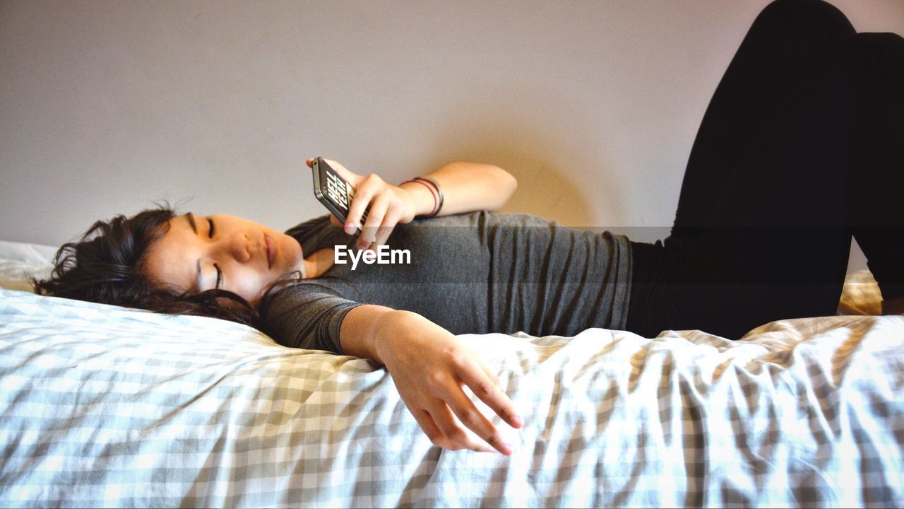 Woman using phone while lying on bed