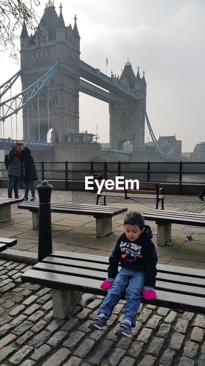 FULL LENGTH OF WOMAN SITTING ON BRIDGE AGAINST SKY