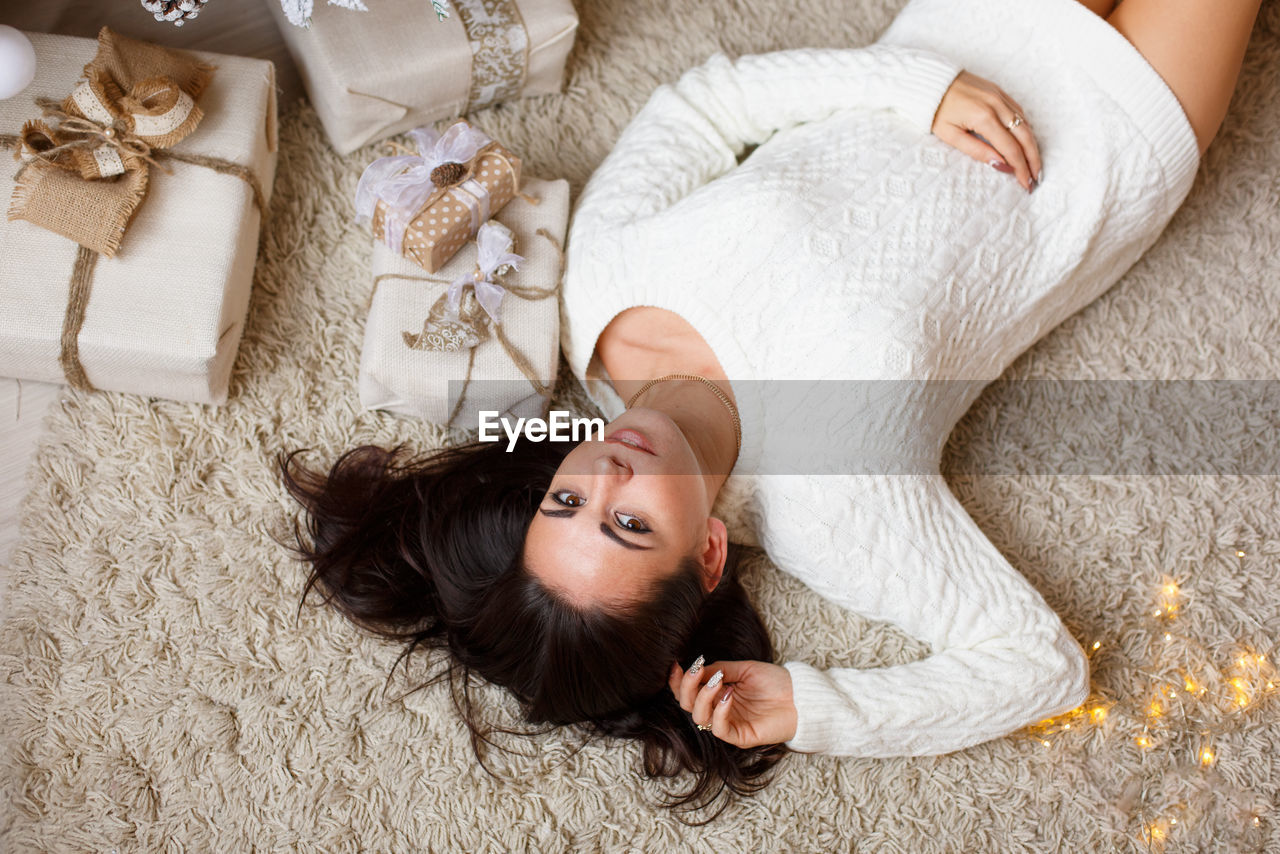 Smiling happy brunette young woman in winter knitted sweater lies on floor