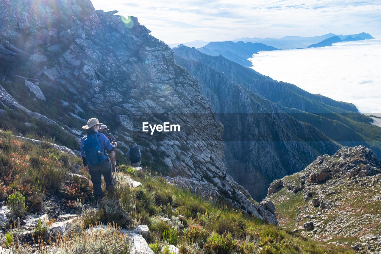 Hikers with backpack trekking down steep hill with clouds and mountain ranges in sight 