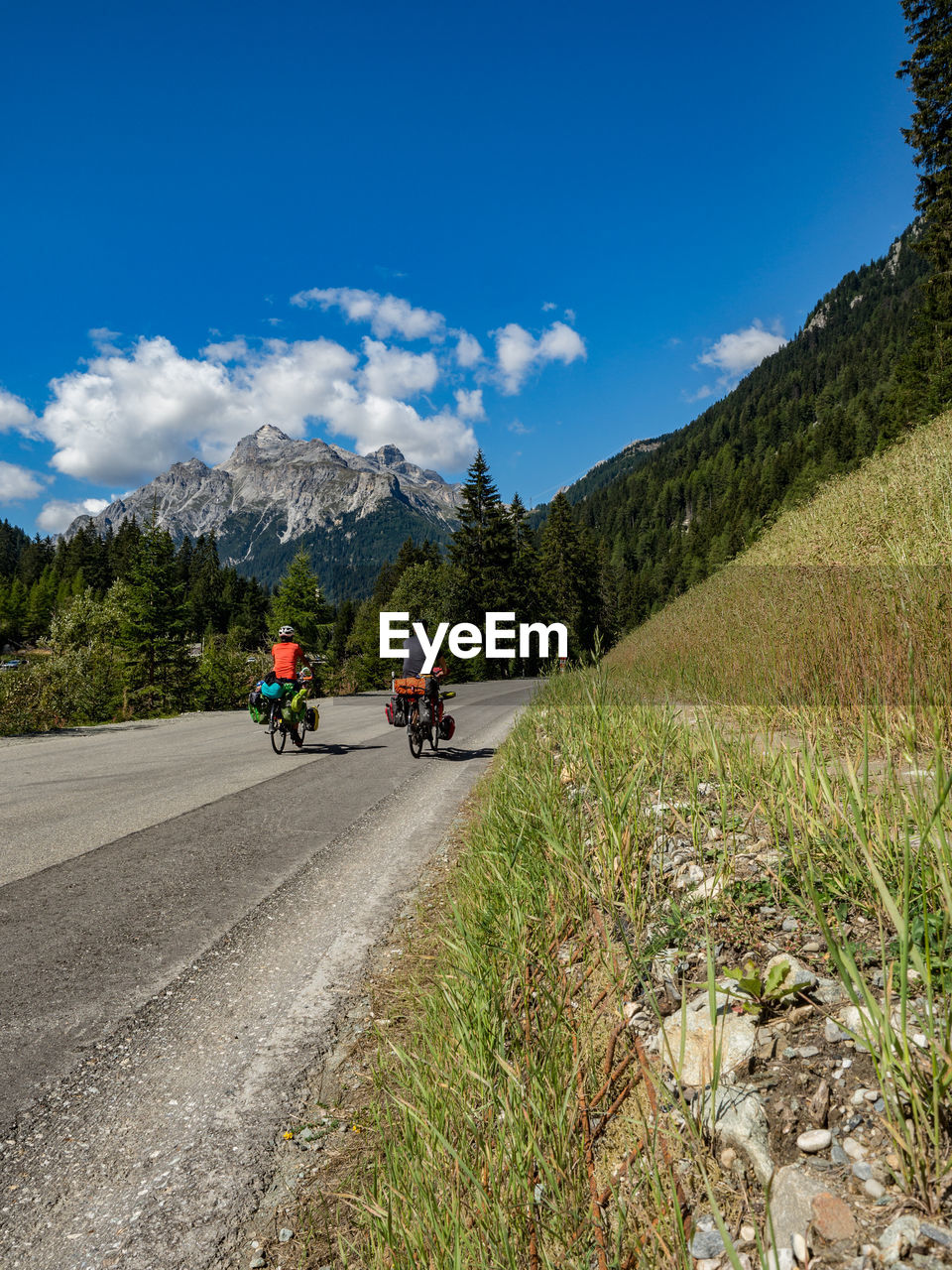 People riding road by mountains against blue sky