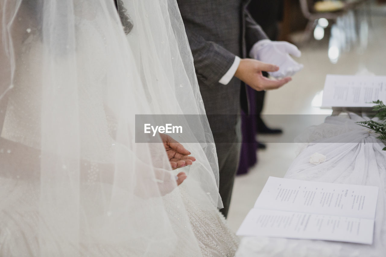 Midsection of heterosexual couple reading vows in wedding hall