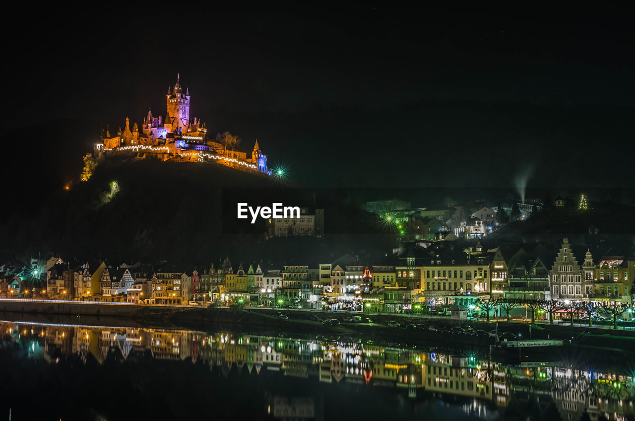 Illuminated buildings reflecting on lake in river at night