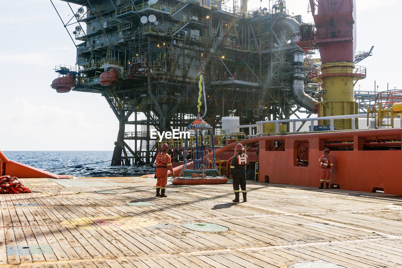 Seamen attending to personal transfer basket at offshore oil field