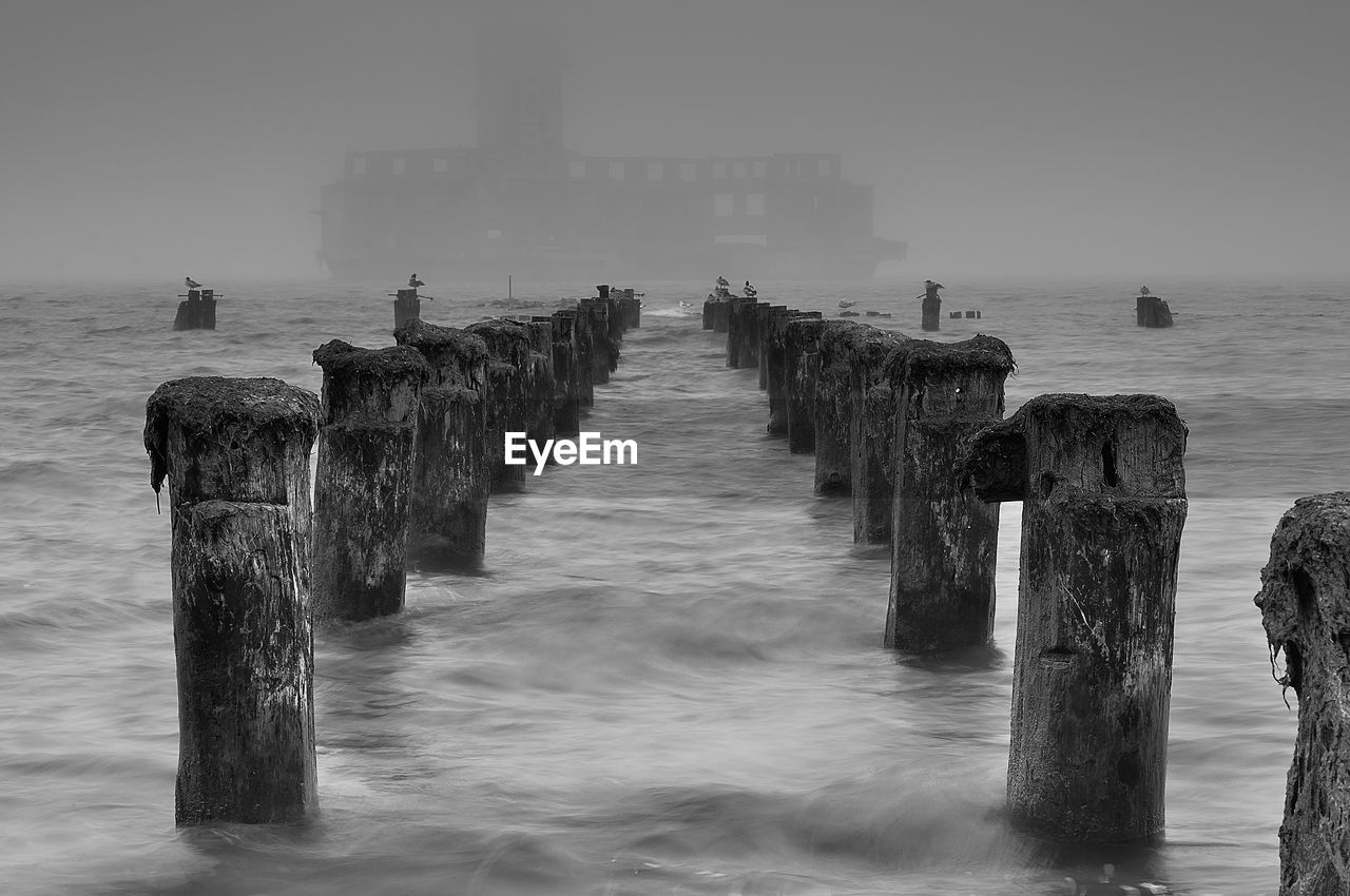 WOODEN POST ON PIER OVER SEA AGAINST SKY