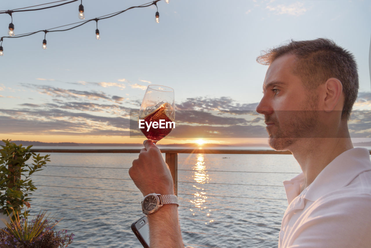 Profile view of mature man having wine against sea during sunset