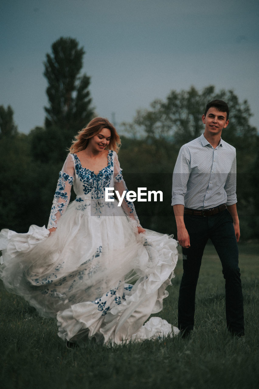 Cheerful couple walking on grass against sky