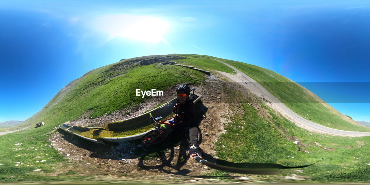 sky, nature, mountain range, activity, mountain, one person, sports, environment, adventure, adult, leisure activity, bicycle, landscape, transportation, sunlight, travel, extreme sports, scenics - nature, beauty in nature, land, full length, day, men, outdoors, travel destinations, green, blue, hiking, paragliding, lifestyles, non-urban scene, helmet, mode of transportation, lens flare, exploration, terrain, motion, person, vacation, air sports, cloud, backpack, tourism, sunny, tranquility